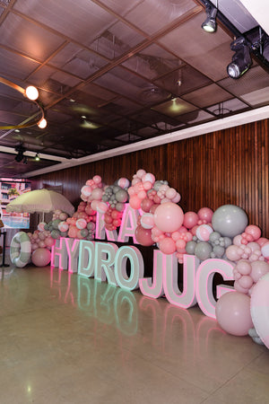 Pastel garden tablescape under a peach and lilac balloon arch, with taper candles, coupe glasses and a grazing board.